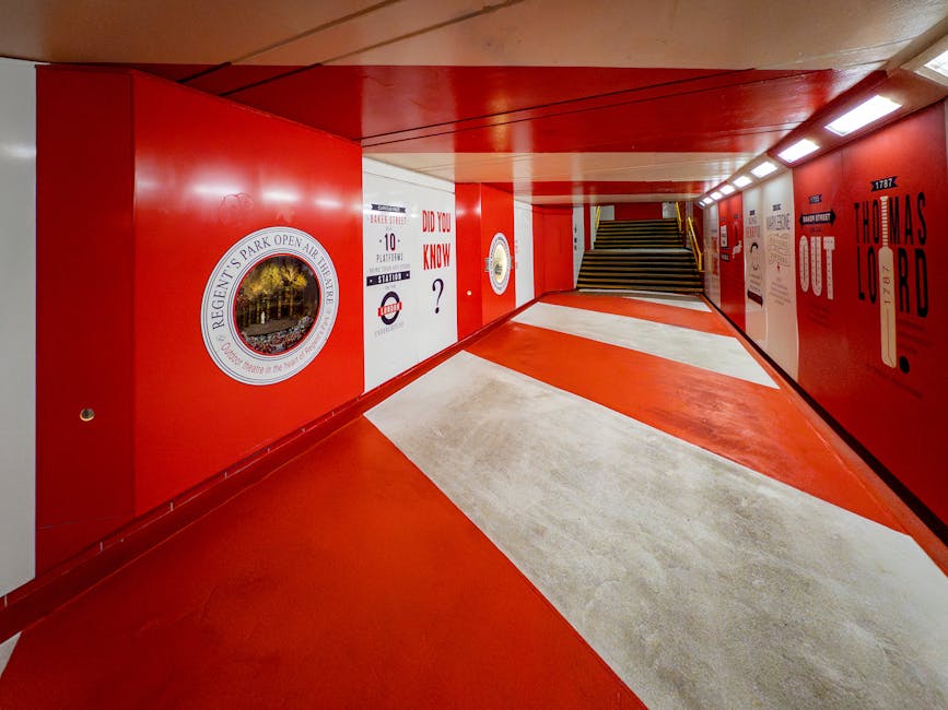 The image shows a vibrant indoor staircase passage painted predominantly in red, with white accents on the steps. The left wall features a circular logo for Regent's Park, and various posters and sign
