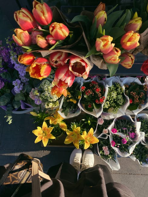 A vibrant display of fresh flowers at a pop-up stall setup for a flower arrangement event on Baker Street, featuring a bouquet of orange and yellow tulips with green stems and leaves, arranged in a na